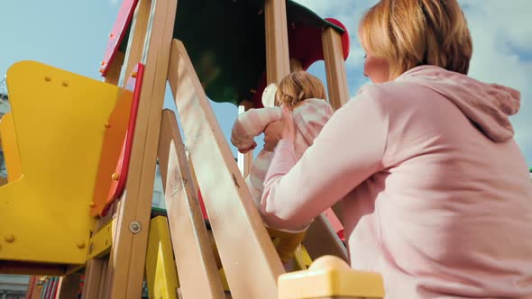 A young mother helps her young child on a children's slide. alt