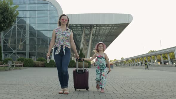 Mother and Daughter Walking From Airport. Woman Carrying Suitcase Bag. Child and Mom After Vacation alt