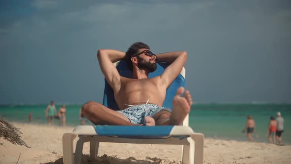 Man Lies On Sunbed.Man Relaxing On Tropical Island Beach.Man Lies On Sunbed On Vacation. alt