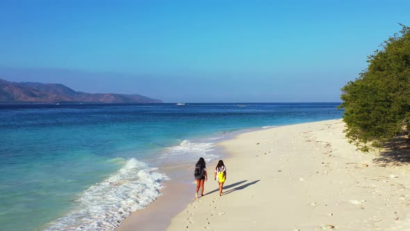 Modern smiling girls travelling by the sea on beach on clean white sand and blue background  alt