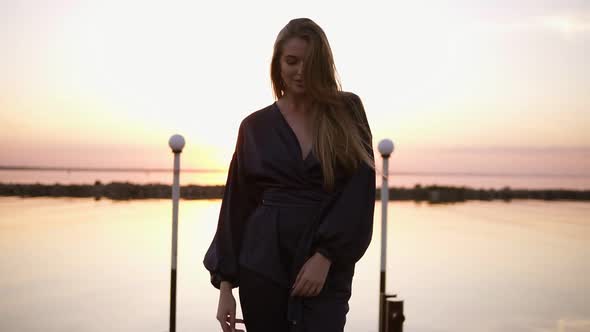 Blonde Haired Young Caucasian Woman Model in Black Clothes Kimono Walking By the Pier alt