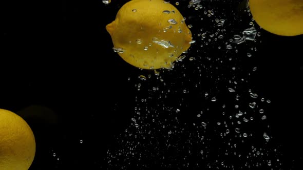 Slow Motion Yellow Lemon Falling Into Transparent Water on Black Background alt