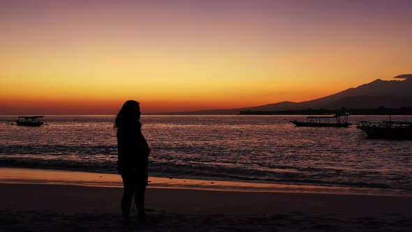 Silhouette of a woman with outstretched hands on the tropical sandy beach during the purple sunset alt