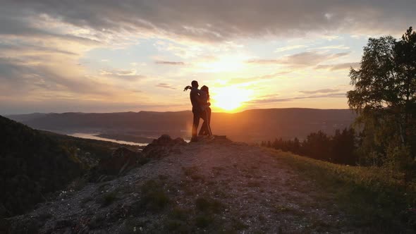 Silhouettes of a Pair of Young Men Kissing on Top of a Mountain at Sunset