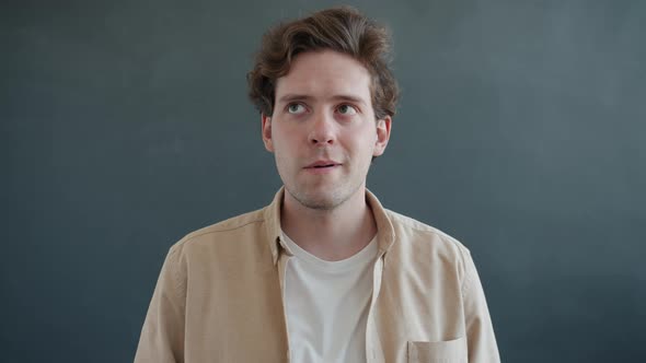 Frustrated Guy Rotating Eyes Looking Around Then Staring at Camera with Confused Face on Gray alt