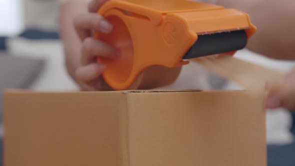 Close up shot of Young Asian Woman Hand Packing, Taping a Cardboard Box