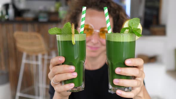 Caucasian Girl Showing to the Camera Two Green Smoothies with Paper Straws alt
