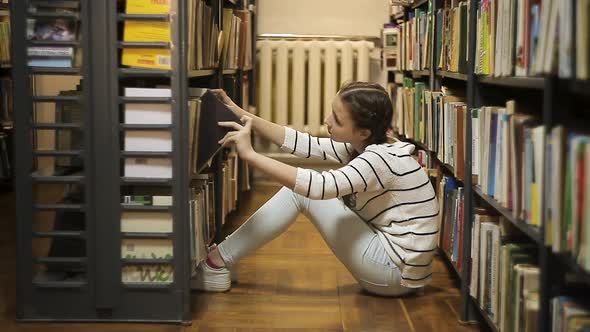 Girl Chooses a Book on a Shelf in the Library, Girl Sitting on the Floor in the Library