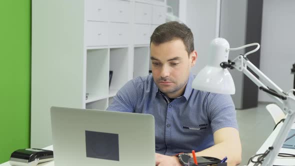 Focused business man entrepreneur typing on laptop doing research. Young male professional alt