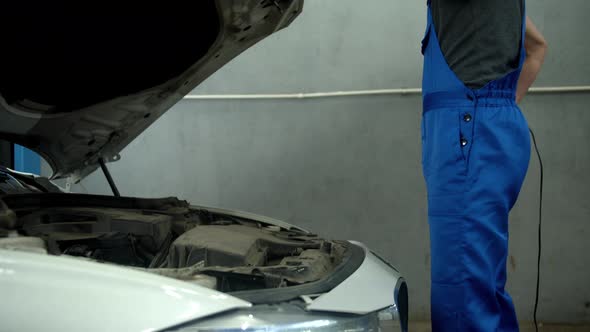 Slow Motion, Mechanic Opens the Hood of a Car and Turns on a Flashlight alt