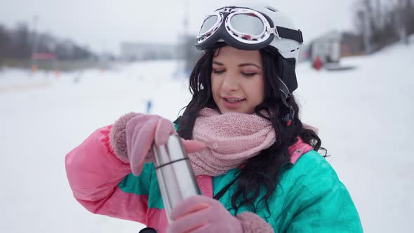 Portrait of Smiling Charming Woman Opening Thermos with Hot Tea at Winter Resort alt