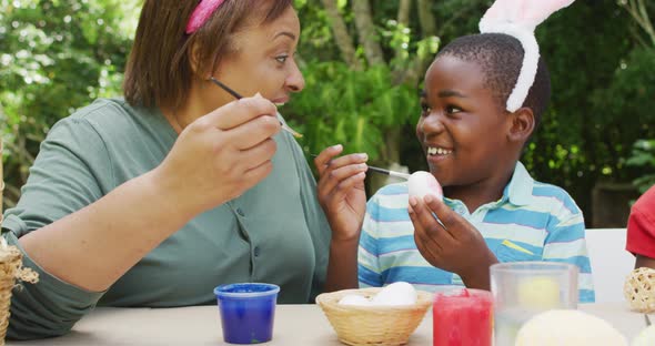 Animation of happy diverse grandmother and grandson painting easter eggs in garden alt
