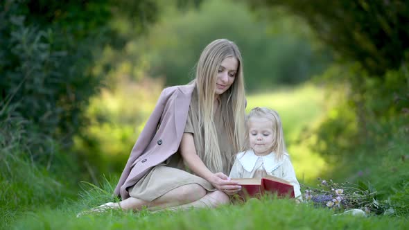 Happy young mum and baby reading a book outdoor beautiful field of sunshine and spring grass