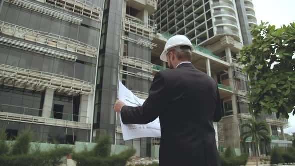 Engineer Male Men Wearing Face Protective Mask Holding a Blueprint of the Building and Working alt