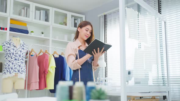 Asian beautiful tailor woman working on clothes in tailoring atelier. alt