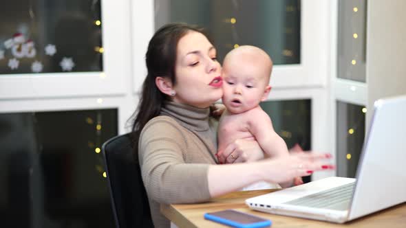 Young Woman with Toddler in Arms Typing on Laptop Remote Work with a Baby at Home