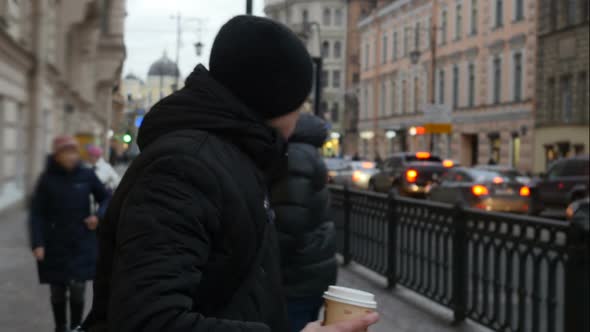 Serious Tired Man In Black Walks On The Street and Drinking a Coffee to Go