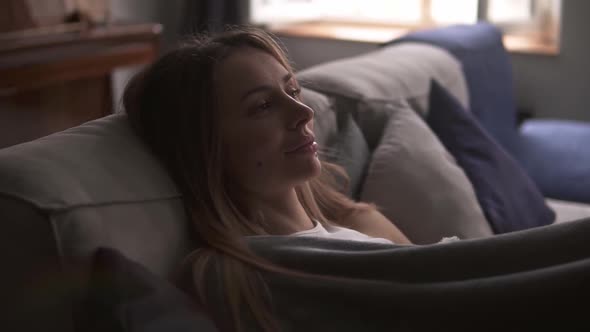Smiling Beautiful Woman Sitting in Room on the Sofa Dreaming of Something Good Wrapped with Plaid alt