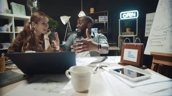 Smiling African American Man Telling Story To Businesswoman Near Laptop Indoors. alt