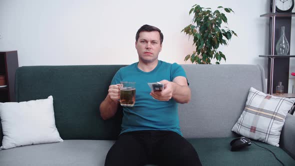 Caucasian man drinks beer while watching TV switching channels