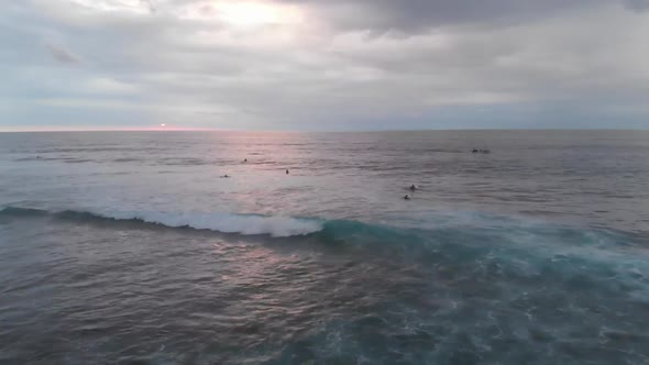 Aerial flyover view of waves crashing during sunset with people swimming in the sea in Bali