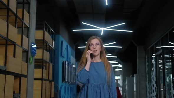 Successful businesswoman walks down corridor and calls on her mobile phone alt