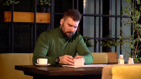 a Serious Bearded Businessman Signs Important Papers Sitting in a Cafe
