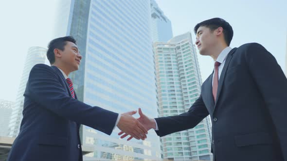 Asian businessmen making handshake after complete the negotiation. Business deal, merger in city. alt