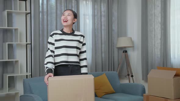 Young Asian Woman Carrying Cardboard Box With Stuff Into A New House Then Looking Around alt