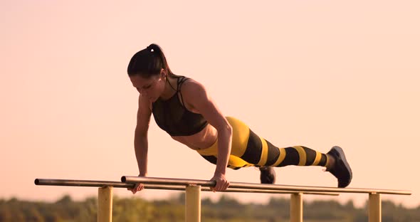 Beautiful Woman Athlete at Sunset Performs Pushups on a Parallel Horizontal Bar alt