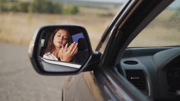 Reflection of Woman in Car Rear View Mirror Who Applying Lip Gloss and Smiling alt