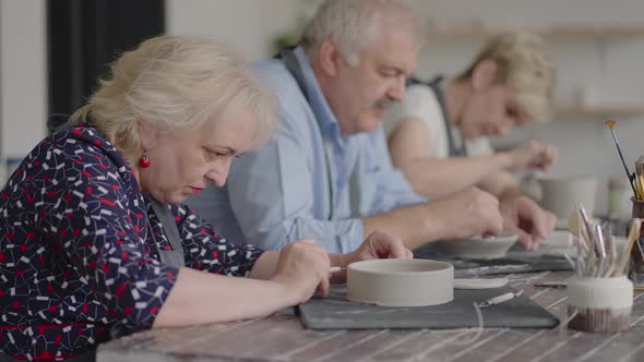 A Group of Elderly People at a Master Class in Pottery Together Sculpt and Cut a Drawing on Cups of alt