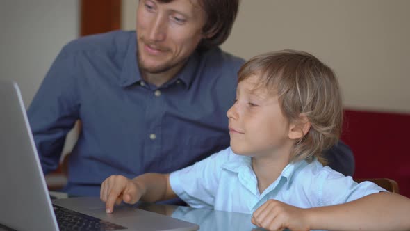 A Young Man and His Little Son Sit a Home During Quarantine and Study in the Internet School Using a alt