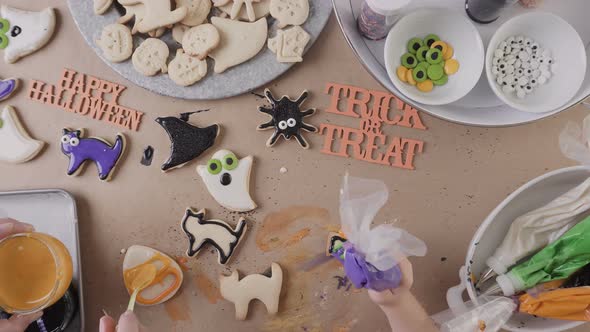 Step by step. Mother and daughter decorating Halloween sugar cookies with colorful royal icing. alt