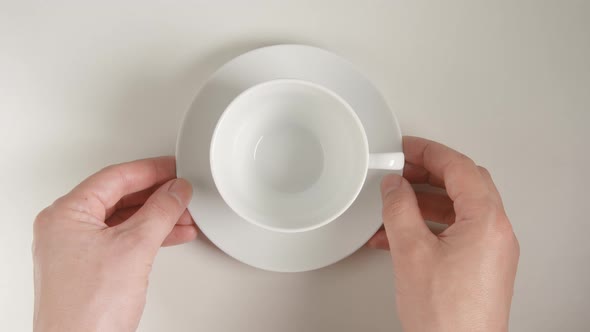 Top View: Human Hands Puts A White Teacup On A White Table