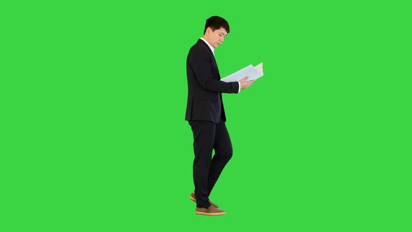 Asian Businessman Walks with Documents Looking at Object on a Green Screen Chroma Key