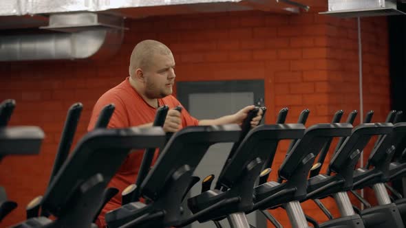 Fat Exhausted Man Working Out on Elliptical Trainer in Gym To Lose Weight