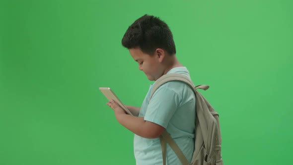 Side View Of Asian Boy Student Use Tablet And Walking To School On Green Screen Chroma Key alt