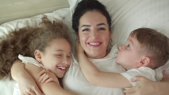 Happy Cute Funny Smiling Laughing Mom and Her Kids Daughter and Son Kiss Their Mom on Cheek Hugging alt