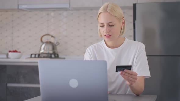 Young Blonde Woman Holds Bank Card and Types Its Details on Laptop