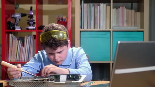 Schoolboy boy solders chip and watches video with instructions in laptop