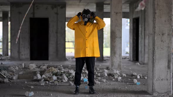 Stalker Survivor Stands in Yellow Raincoat and Black Gas Mask in Abandoned Building and Wears Hood alt