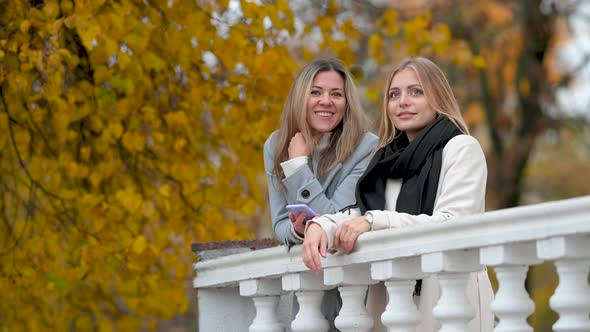 Two happy girls with a phone are resting in an autumn park