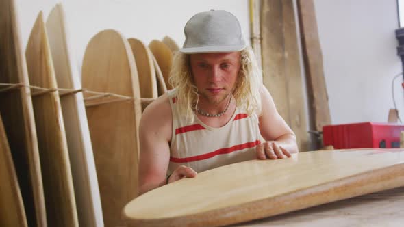 Caucasian male surfboard maker checking one of the surfboards in his studio alt
