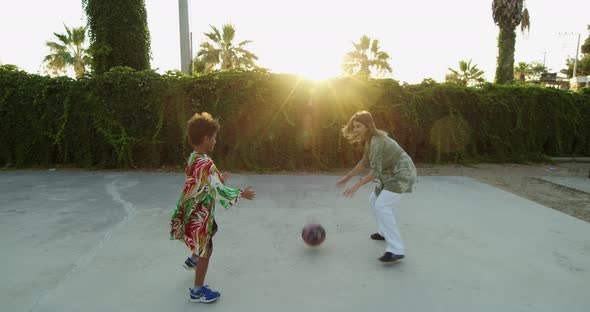 a Mother and Her Child Play Basketball on a Playground Covered with Greenery alt