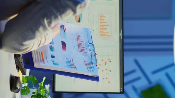 Vertical Video Back View of Manager Analysing Graphics From Clipboard at Midnight alt