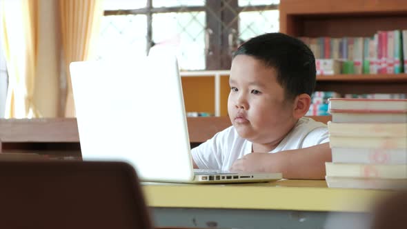 Little asian boy studying online from home watching web class lesson or listening tutor by video cal alt