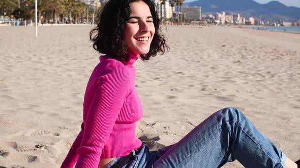 Young Woman Smiling on the Beach Sitting Against the Background of the Sea