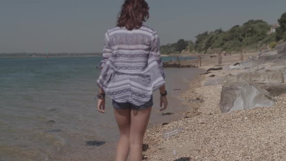 Young Woman Walks Along Beach and Picks Up Plastic Bottle - Ungraded alt