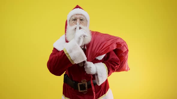 Santa Claus with red sack keeping forefinger by his mouth and looking at camera. Shh! Confidential.